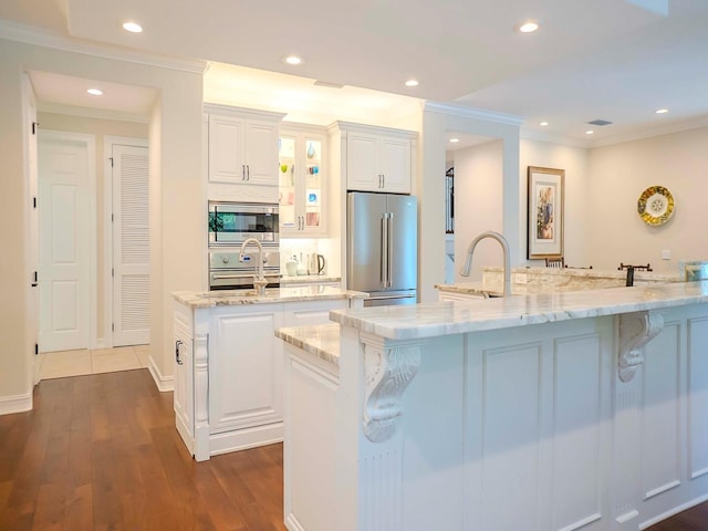 kitchen featuring light stone countertops, a large island with sink, white cabinets, and appliances with stainless steel finishes