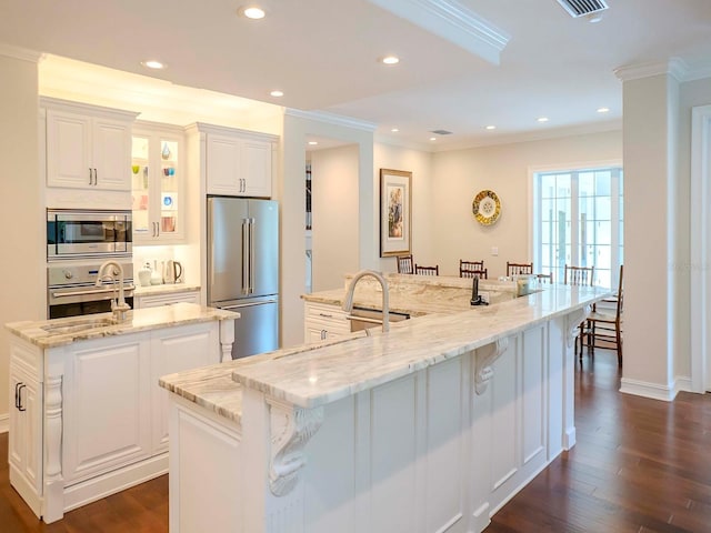 kitchen featuring dark wood-type flooring, stainless steel appliances, a spacious island, light stone counters, and white cabinets