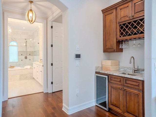 bar with sink, light stone counters, hanging light fixtures, dark hardwood / wood-style flooring, and beverage cooler