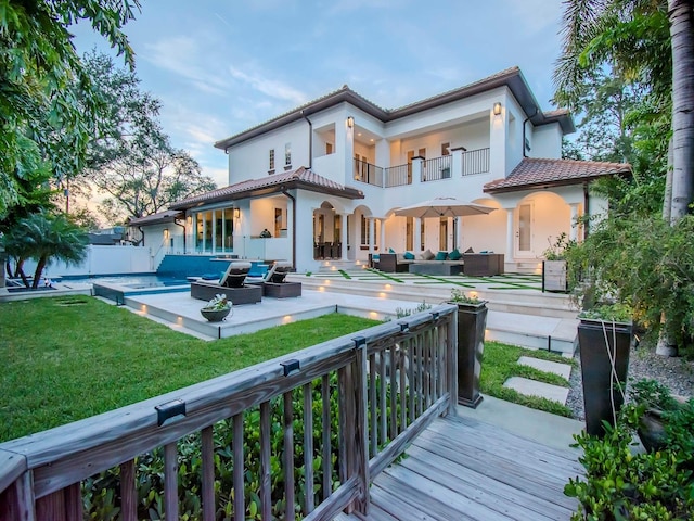 rear view of property with a pool side deck, a balcony, an outdoor living space, and a yard