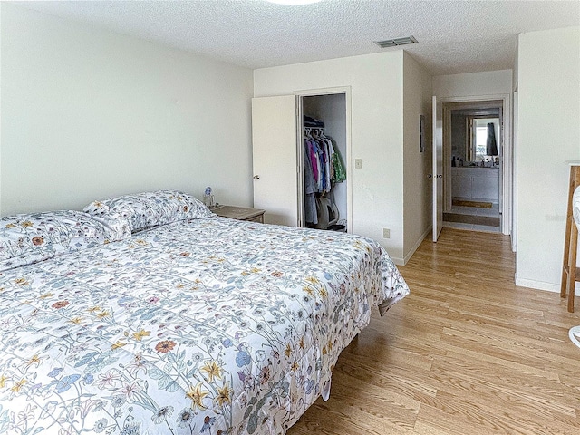 bedroom featuring a walk in closet, a textured ceiling, light hardwood / wood-style floors, and a closet