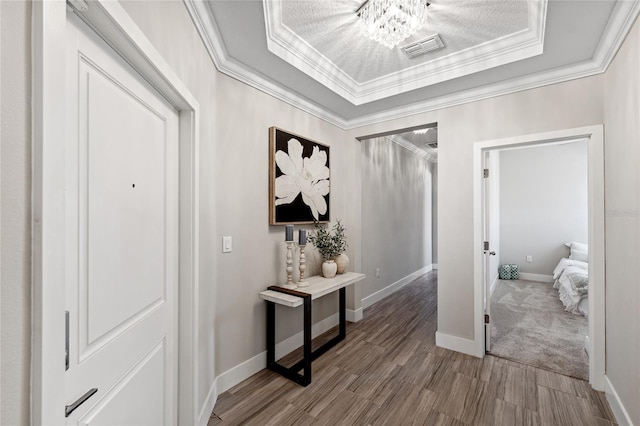 corridor with ornamental molding, a tray ceiling, and wood-type flooring