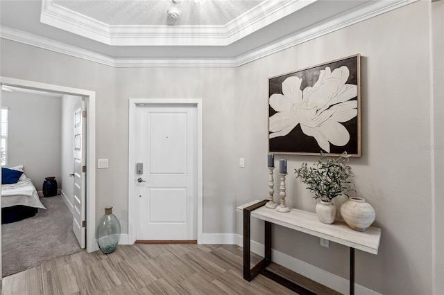 foyer entrance with a raised ceiling, crown molding, and light wood-type flooring