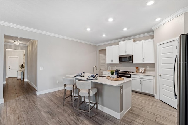 kitchen with appliances with stainless steel finishes, a breakfast bar, white cabinets, ornamental molding, and a kitchen island with sink