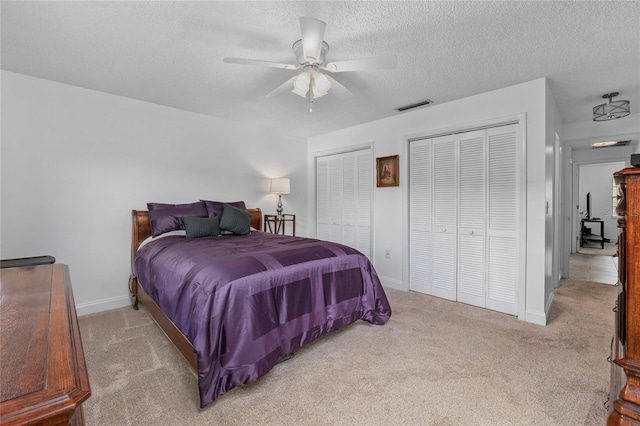 bedroom with two closets, light colored carpet, and a textured ceiling