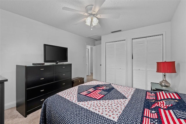 bedroom featuring multiple closets, ceiling fan, light colored carpet, and a textured ceiling