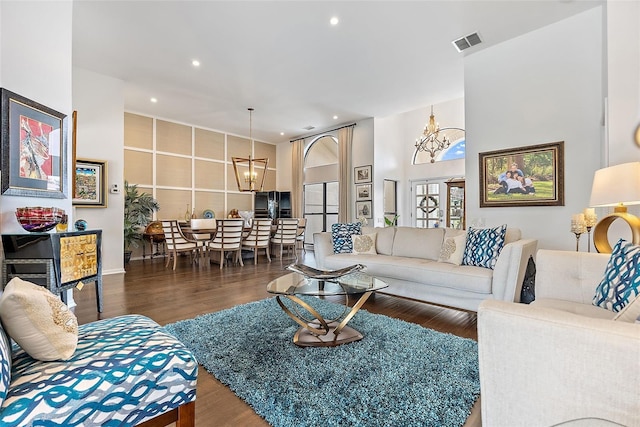 living room with dark hardwood / wood-style floors, an inviting chandelier, and a towering ceiling