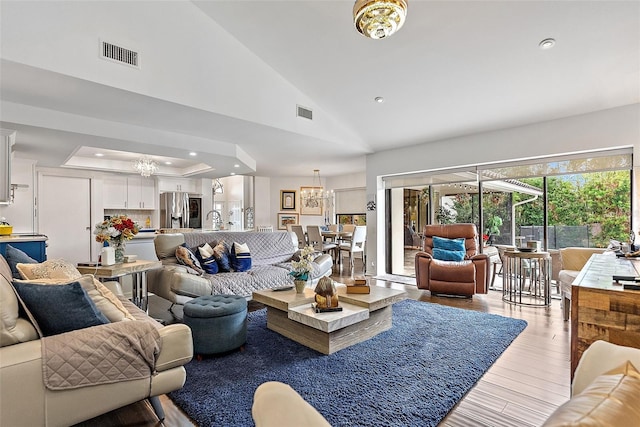 living room with a tray ceiling, high vaulted ceiling, a chandelier, and light wood-type flooring