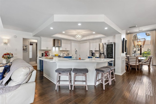 kitchen featuring white cabinetry, wall chimney range hood, a large island with sink, and a chandelier