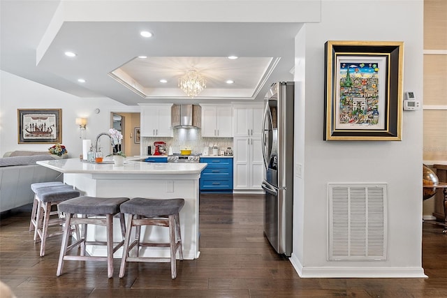 kitchen featuring an island with sink, white cabinetry, a breakfast bar area, stainless steel fridge, and wall chimney exhaust hood