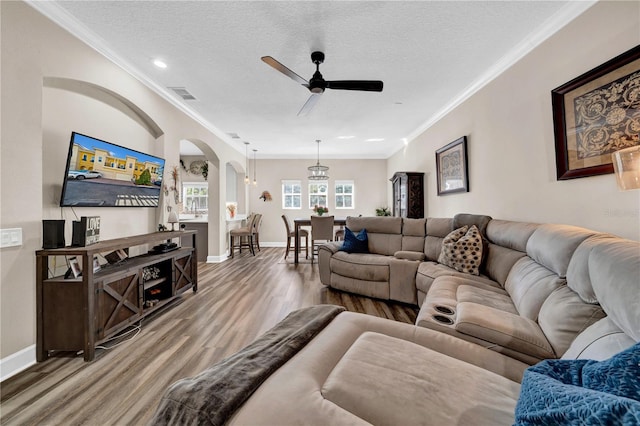 living room featuring ceiling fan, hardwood / wood-style flooring, ornamental molding, and a textured ceiling