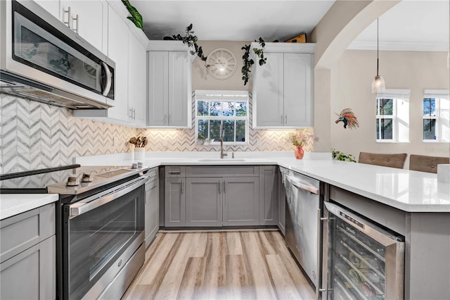 kitchen with sink, appliances with stainless steel finishes, gray cabinetry, kitchen peninsula, and beverage cooler