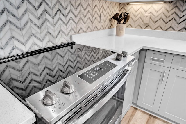 details with white cabinetry, stainless steel electric range oven, decorative backsplash, and light wood-type flooring