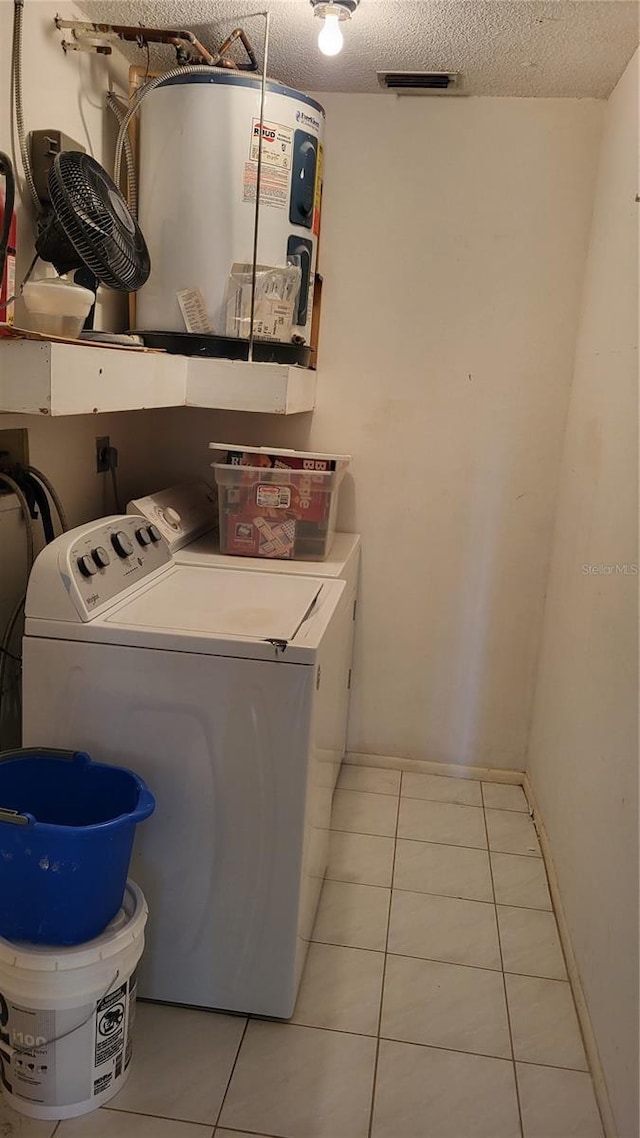 laundry room featuring a textured ceiling, electric water heater, washer and dryer, and light tile patterned floors