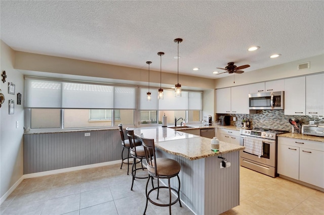 kitchen featuring hanging light fixtures, appliances with stainless steel finishes, white cabinets, and a kitchen breakfast bar