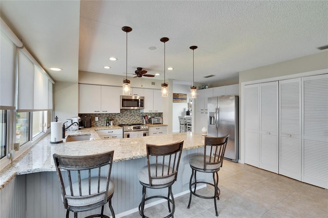 kitchen featuring sink, light stone counters, appliances with stainless steel finishes, pendant lighting, and white cabinets