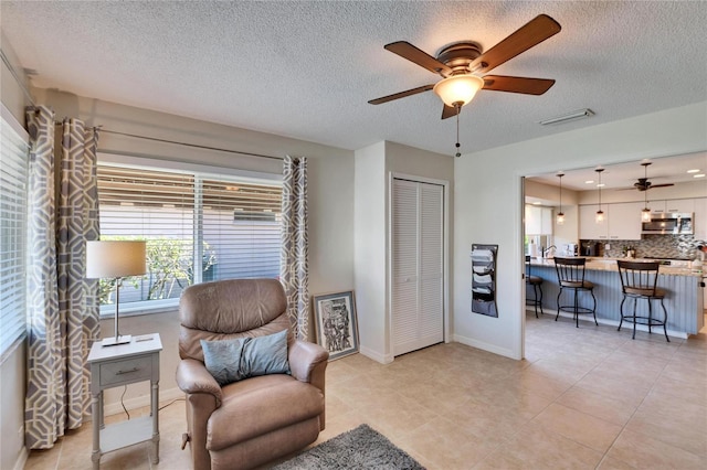 sitting room with ceiling fan, a textured ceiling, and light tile patterned flooring