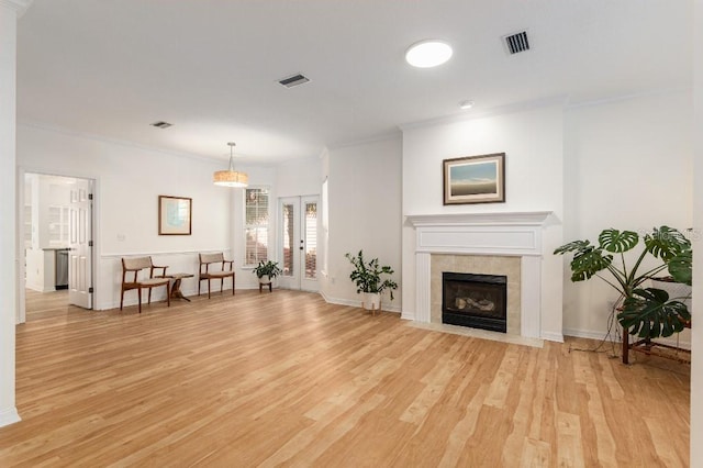 living room with crown molding, a tiled fireplace, light hardwood / wood-style flooring, and french doors