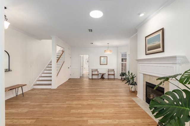 living room with a tiled fireplace, crown molding, and light hardwood / wood-style flooring