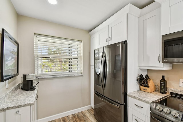 kitchen featuring appliances with stainless steel finishes, white cabinets, light stone counters, and light hardwood / wood-style flooring