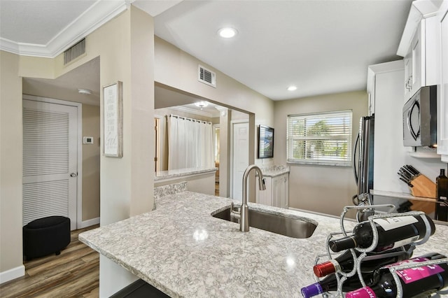 kitchen with sink, appliances with stainless steel finishes, white cabinetry, light stone counters, and dark hardwood / wood-style flooring