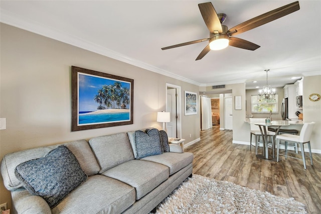 living room with crown molding, ceiling fan with notable chandelier, and light hardwood / wood-style flooring