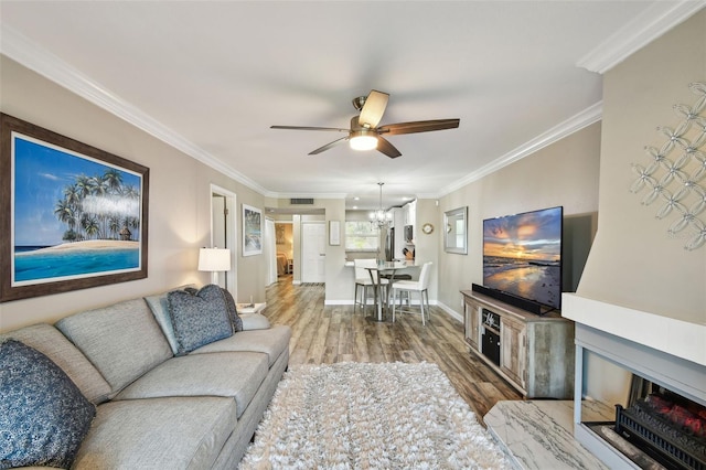 living room with hardwood / wood-style floors, crown molding, and ceiling fan with notable chandelier