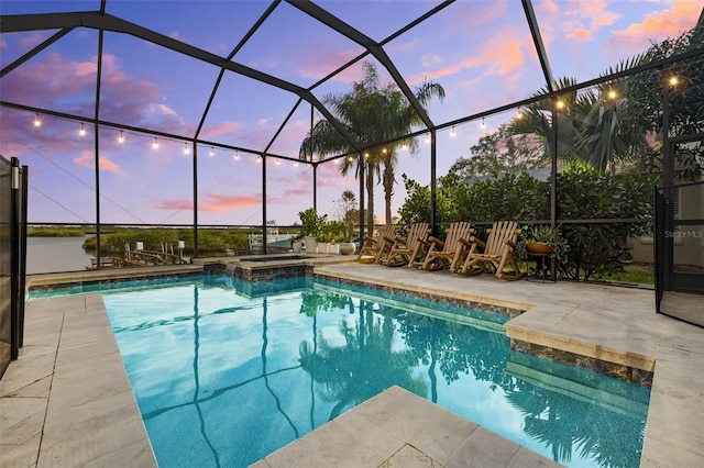 pool at dusk with an in ground hot tub, a water view, a lanai, and a patio area