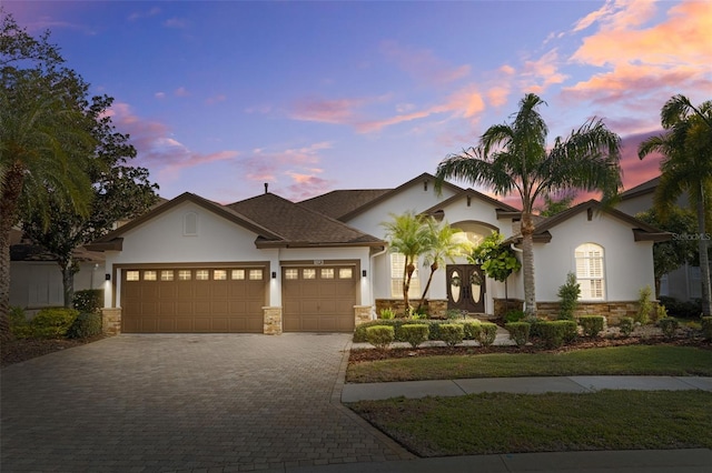 view of front facade with decorative driveway, stone siding, an attached garage, and stucco siding