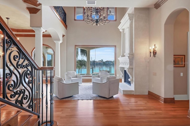 interior space featuring hardwood / wood-style flooring, a towering ceiling, decorative columns, a water view, and a high end fireplace