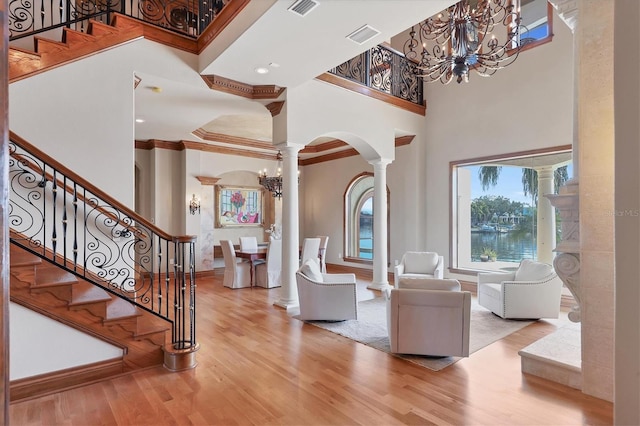 foyer entrance with a notable chandelier, a towering ceiling, light hardwood / wood-style flooring, and ornate columns