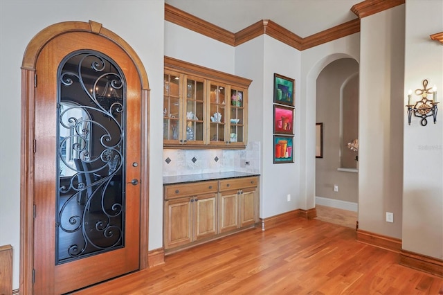 bar with crown molding, light hardwood / wood-style floors, decorative backsplash, and dark stone counters