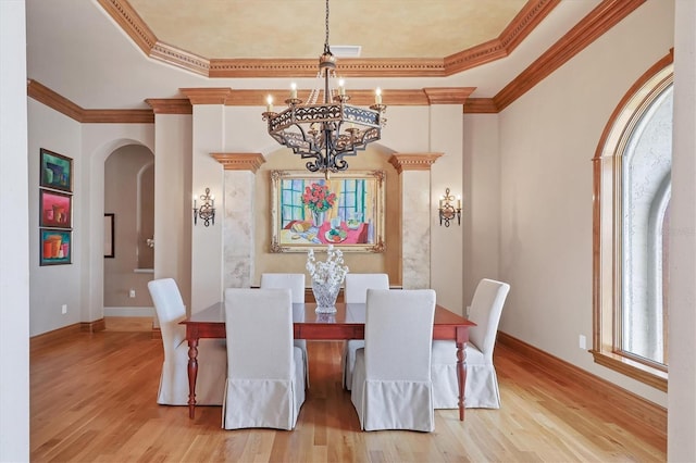 dining area with crown molding, a chandelier, a raised ceiling, and light hardwood / wood-style floors