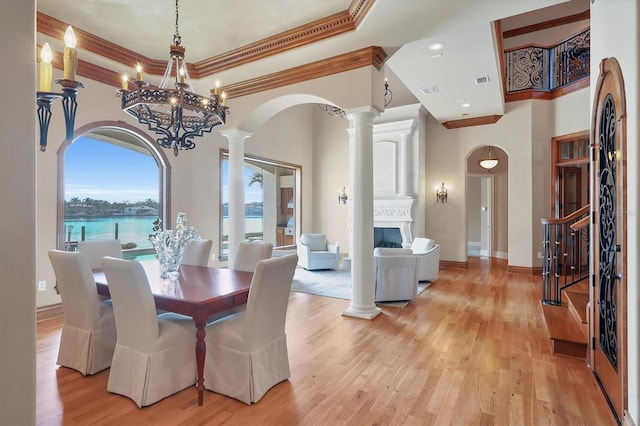 dining area featuring decorative columns, a water view, a towering ceiling, a fireplace, and light hardwood / wood-style floors