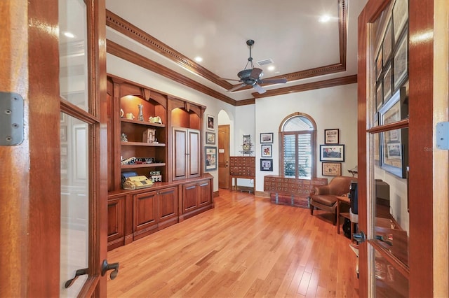 home office featuring light hardwood / wood-style flooring, ornamental molding, a tray ceiling, built in features, and ceiling fan