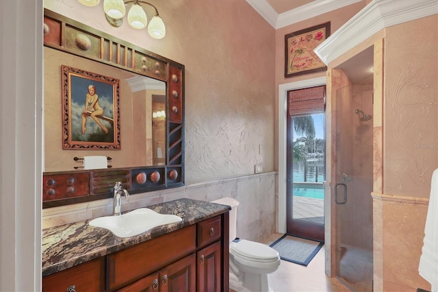 bathroom featuring a shower with shower door, tile walls, vanity, toilet, and crown molding