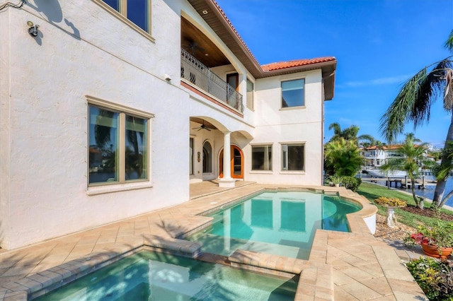 back of property with ceiling fan, a balcony, a swimming pool with hot tub, and a patio area