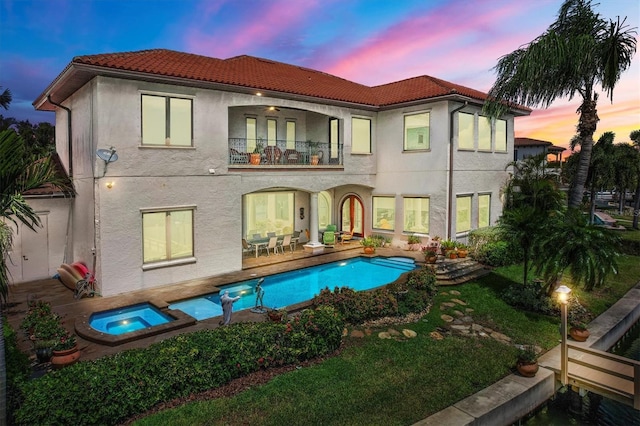 back house at dusk with a patio, a balcony, ceiling fan, and a pool with hot tub