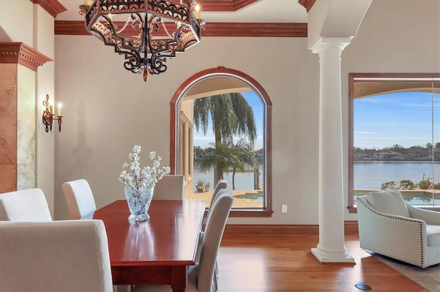 dining space with a water view, ornamental molding, wood-type flooring, and decorative columns