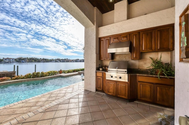 view of pool with a water view, a grill, exterior kitchen, and a patio area