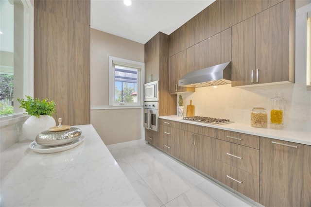 kitchen featuring stainless steel appliances, tasteful backsplash, light stone countertops, and wall chimney range hood