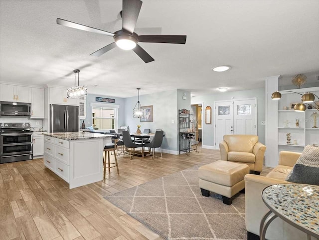 living room featuring ceiling fan with notable chandelier, light hardwood / wood-style flooring, and a textured ceiling