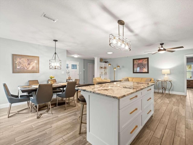 kitchen with a breakfast bar, a center island, light stone counters, white cabinets, and decorative light fixtures