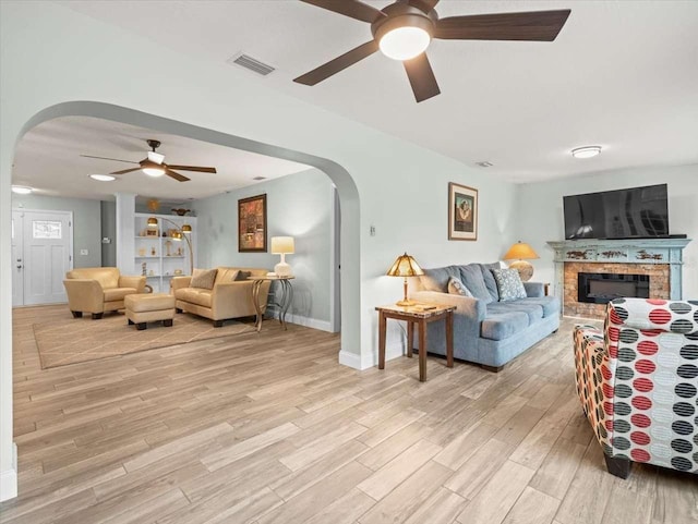 living room with a brick fireplace, light hardwood / wood-style flooring, and ceiling fan