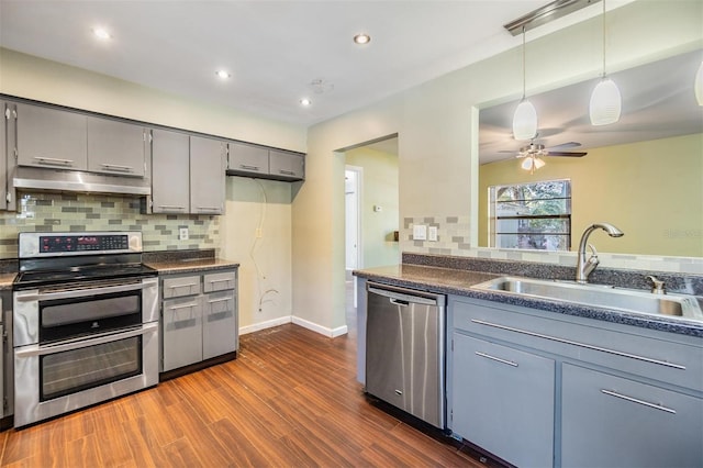 kitchen with sink, dark wood-type flooring, gray cabinets, appliances with stainless steel finishes, and tasteful backsplash