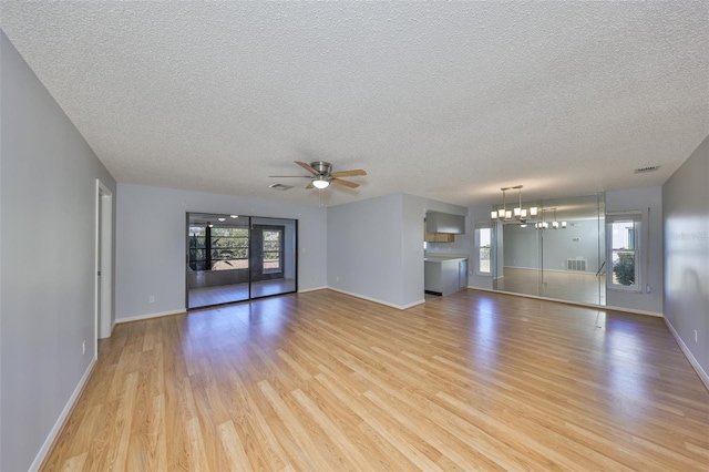 unfurnished living room with plenty of natural light, ceiling fan with notable chandelier, a textured ceiling, and light hardwood / wood-style flooring