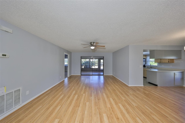 unfurnished living room with ceiling fan, a textured ceiling, a healthy amount of sunlight, and light wood-type flooring