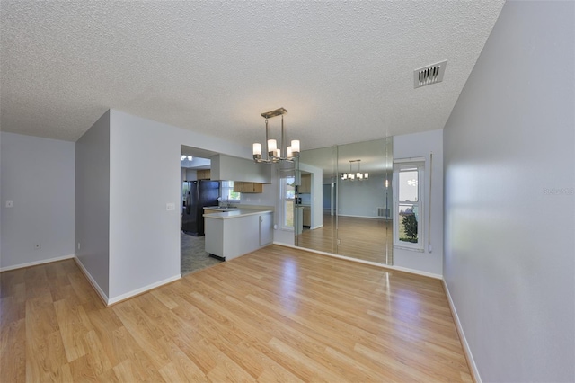 kitchen featuring kitchen peninsula, decorative light fixtures, a notable chandelier, black fridge with ice dispenser, and light hardwood / wood-style floors