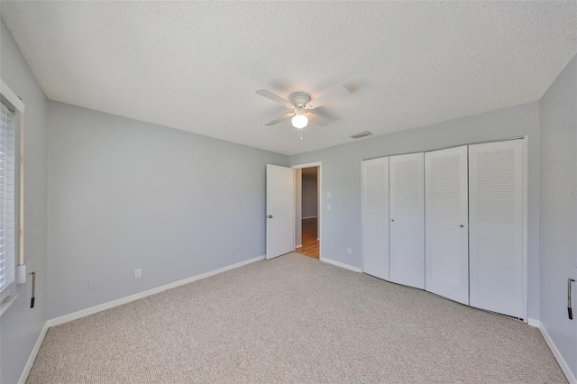 unfurnished bedroom with ceiling fan, light carpet, a textured ceiling, and a closet