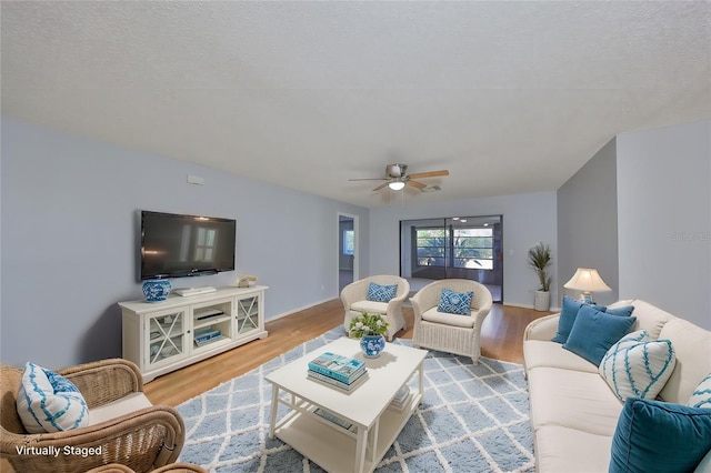 living room featuring ceiling fan, a textured ceiling, and light wood-type flooring